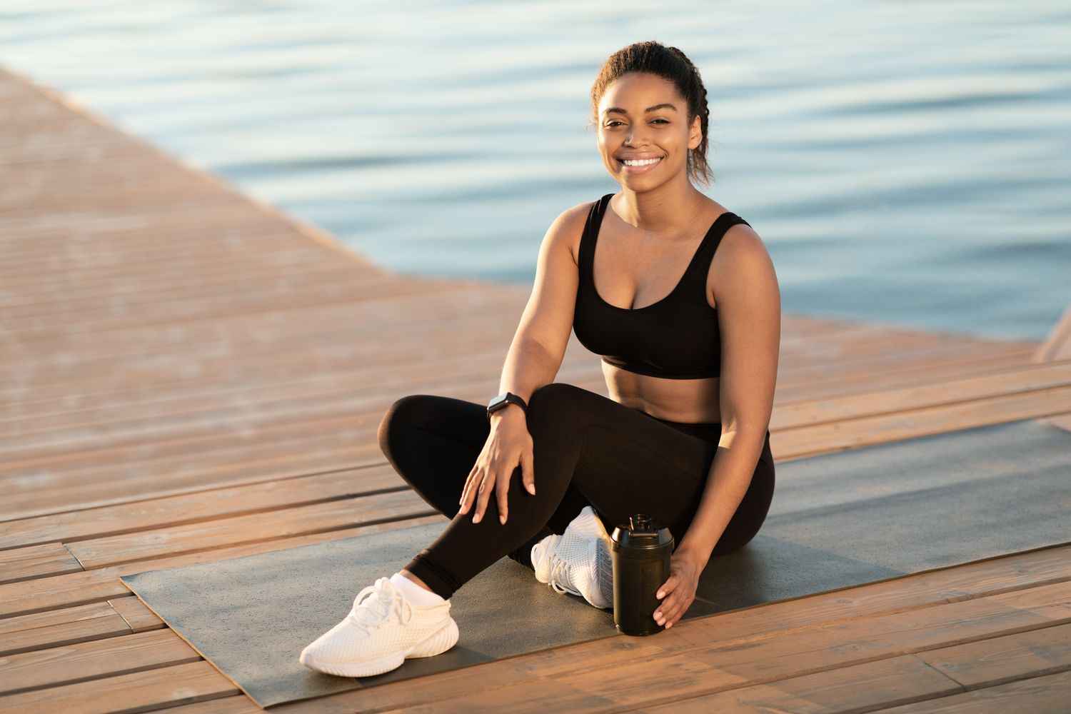 Smiling woman in activewear on waterfront yoga mat.
